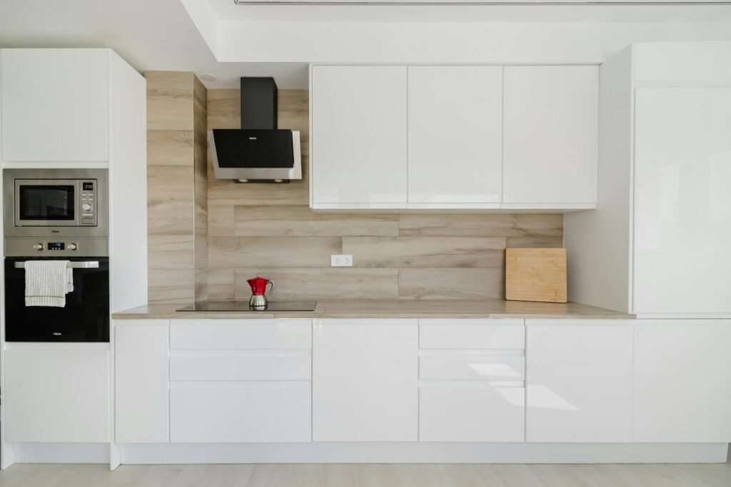 Cocina blanca moderna minimalista con frentes lacados, encimera blanca y campana negra contrastando con madera — Presenti Mobiliario Zaragoza