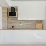 Cocina blanca moderna minimalista con frentes lacados, encimera blanca y campana negra contraste sobre madera