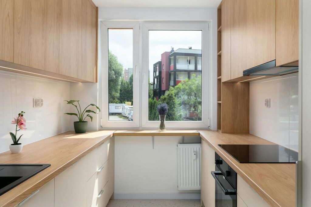 Cocina pequeña en U con frentes blancos, módulos altos en madera y ventana panorámica — fabricada por Presenti Mobiliario en Zaragoza
