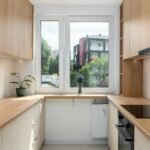 Cocina pequeña en U con frentes blancos abajo, módulos altos en madera y ventana central panorámica
