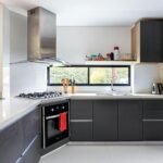 Cocina con distribución en L gris oscuro y blanco con campana inox cilíndrica y ventana panorámica